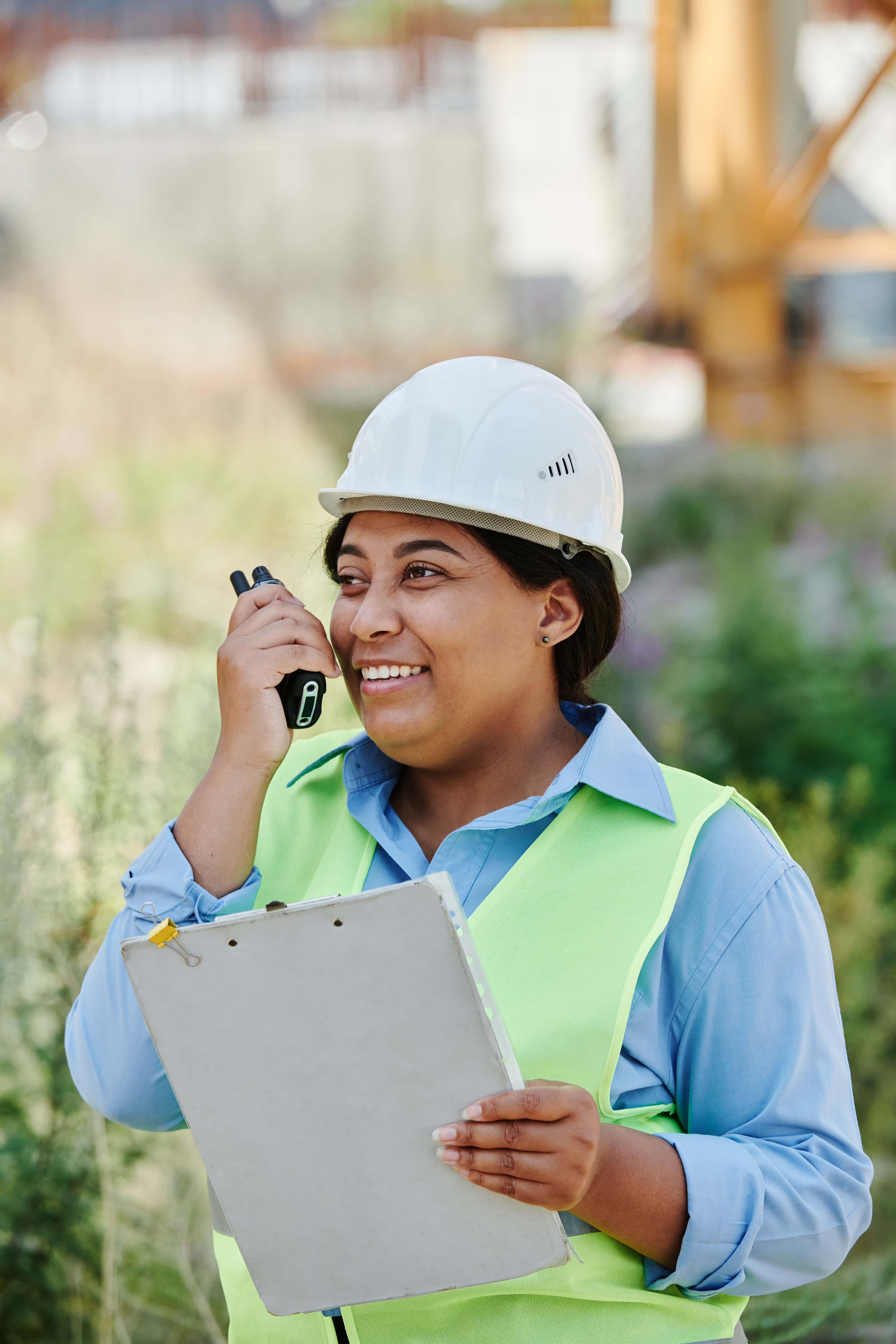 Female engineer with hard hat and walkie talkie at construction site