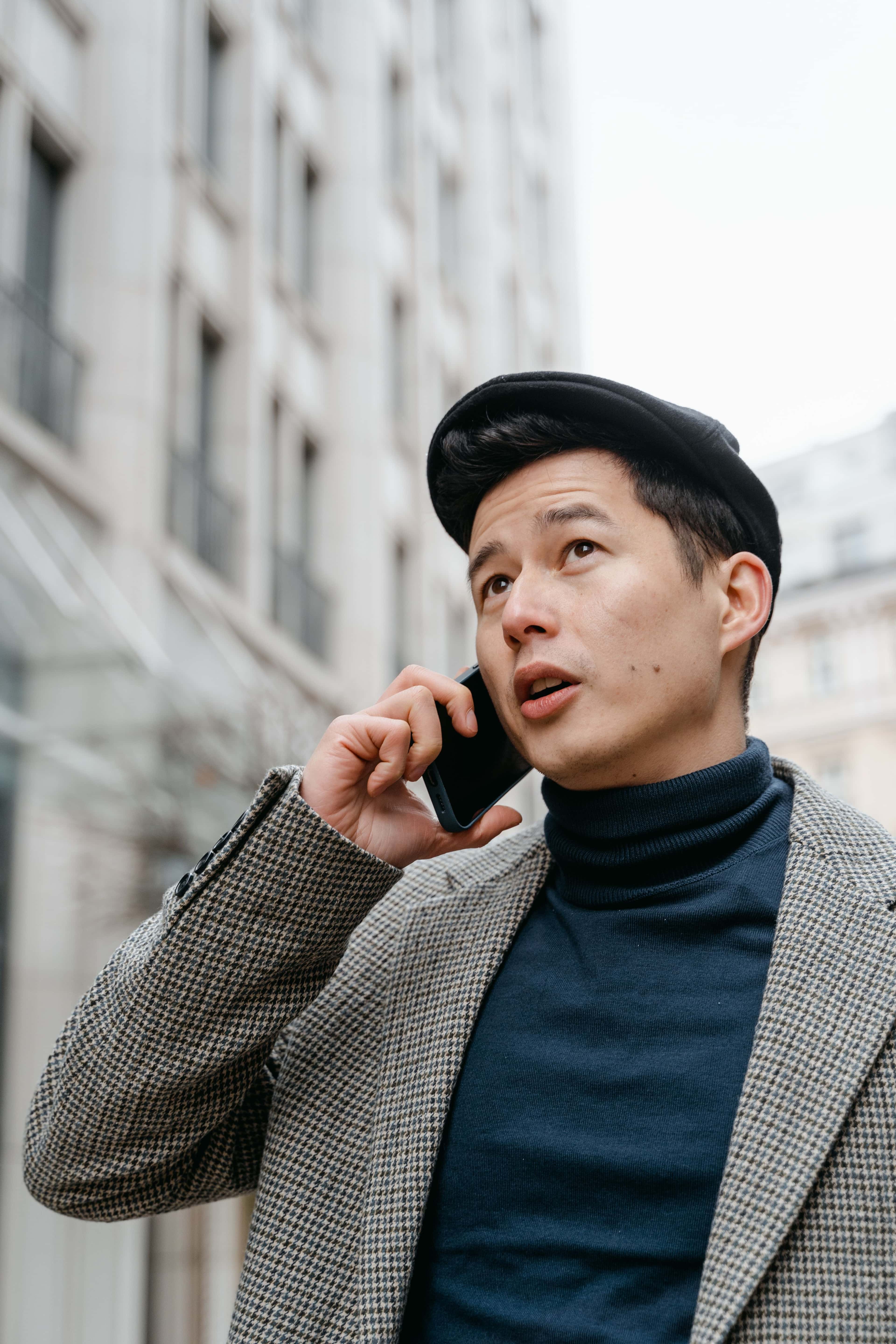 Stylish man in a city talking on a smartphone outdoors, wearing a coat and hat